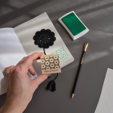 The stamp beside a stamped book, showcasing its modern honeycomb design and personalized text.