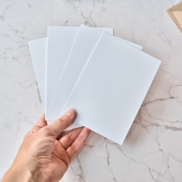 A set of 10 white postcards neatly stacked beside 10 Kraft envelopes on a marbre surface.